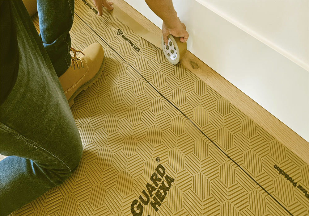 Worker kneeling while taping down Gator Guard Gold heavy-duty floor protection on hardwood
